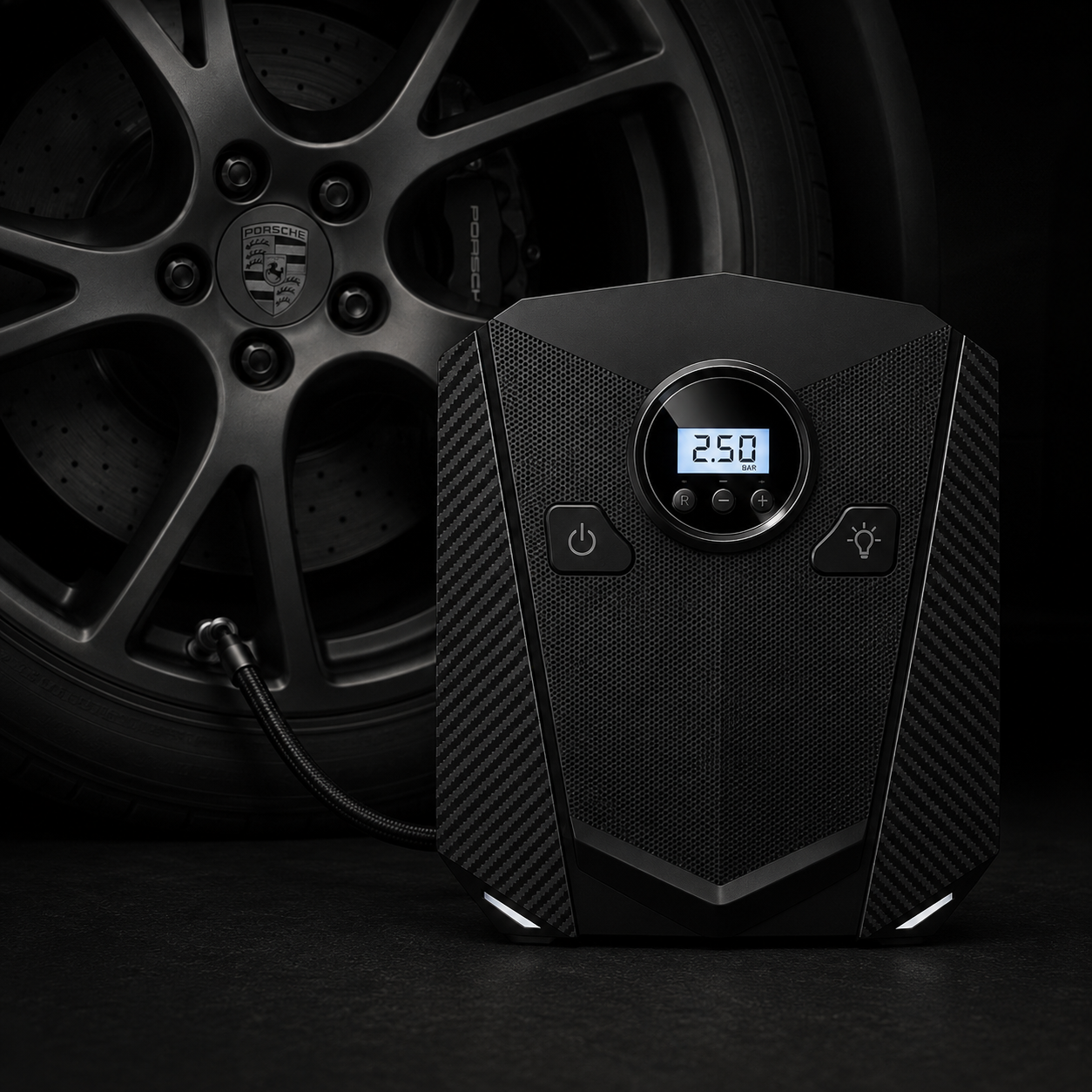Black portable air pump with a digital LCD display showing 2.5 bar, positioned in front of a dark car wheel with a tire inflation hose connected.