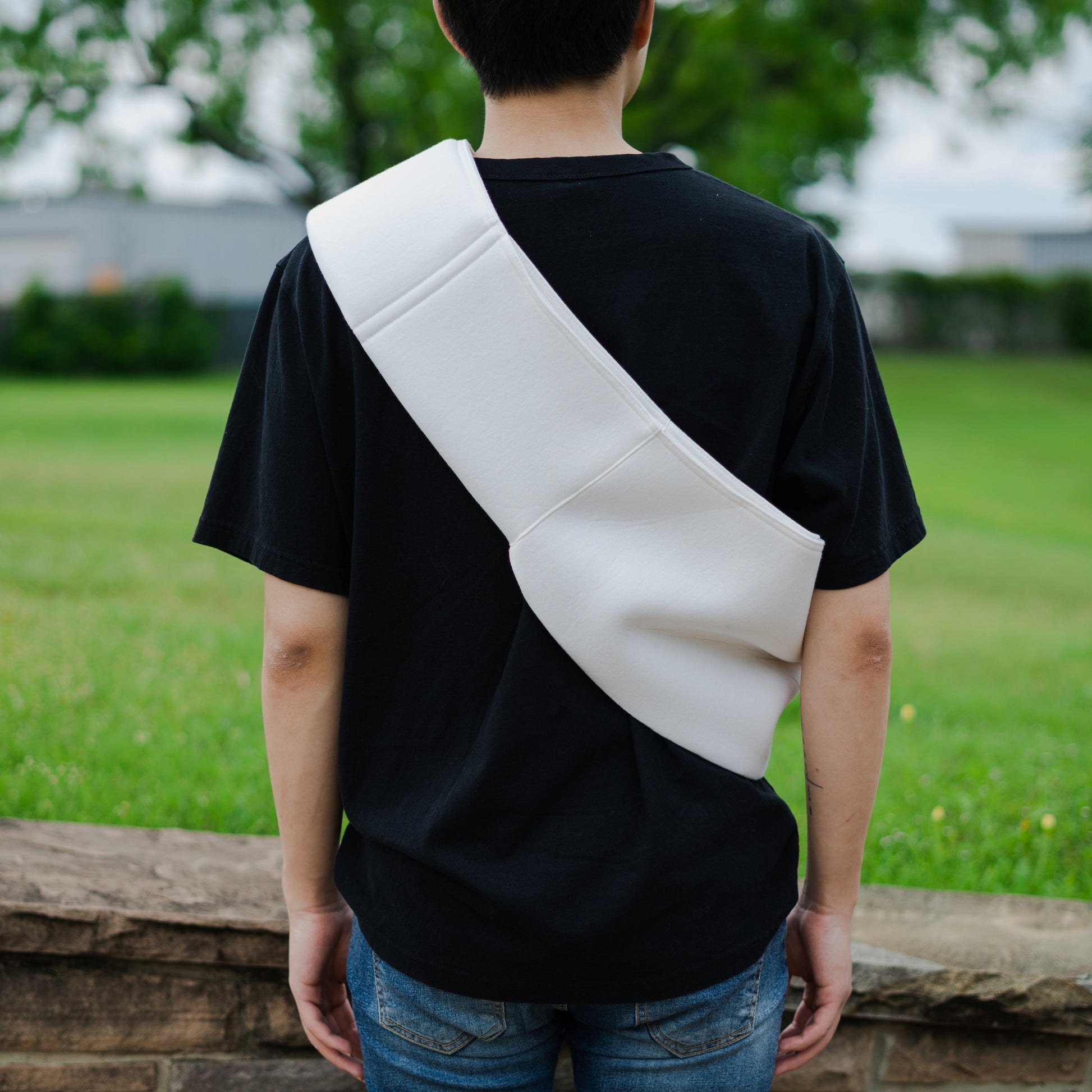 Person wearing a black t-shirt with a white diagonal strap over one shoulder, standing outdoors.