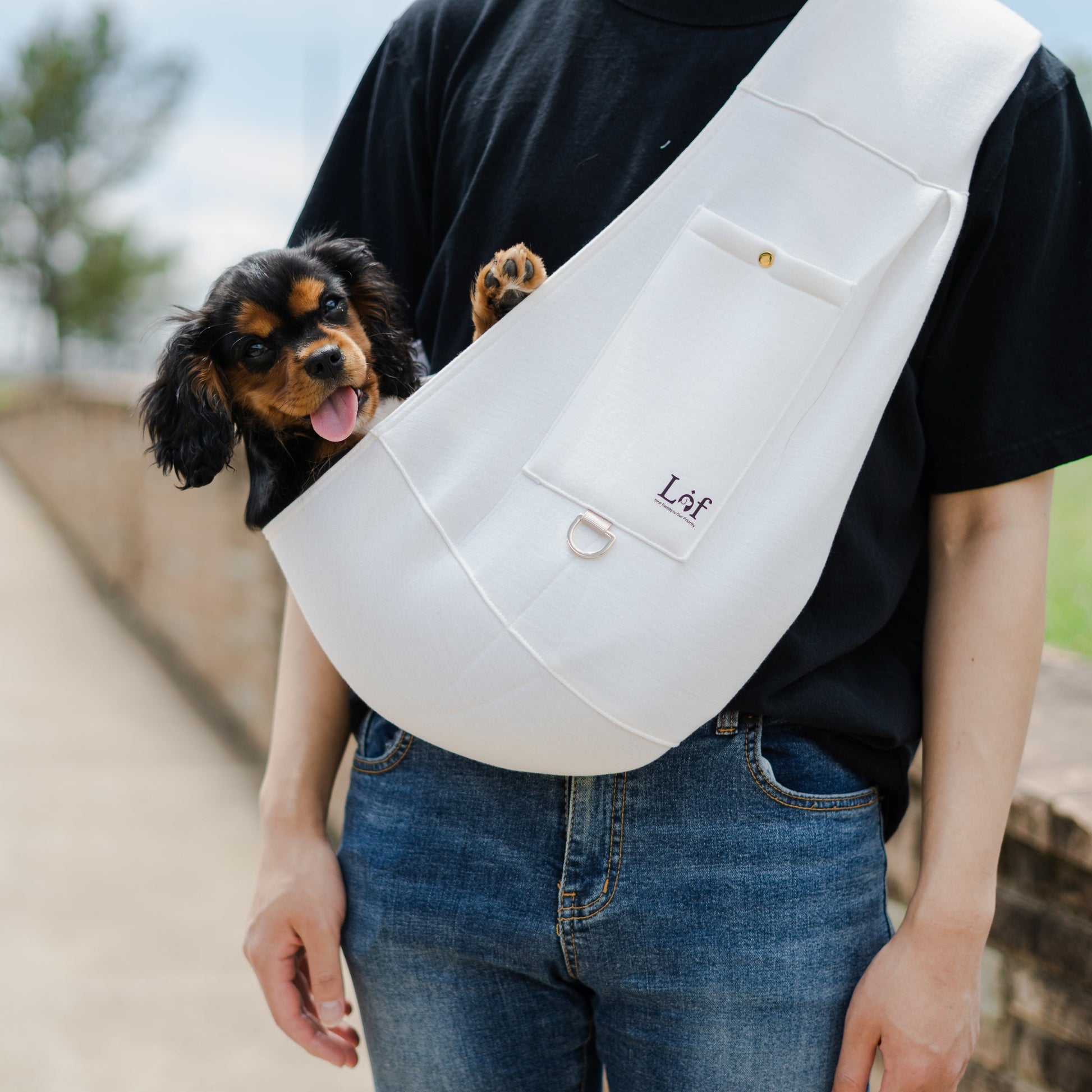 Person carrying a small dog in a white sling with 'Lof' branding.