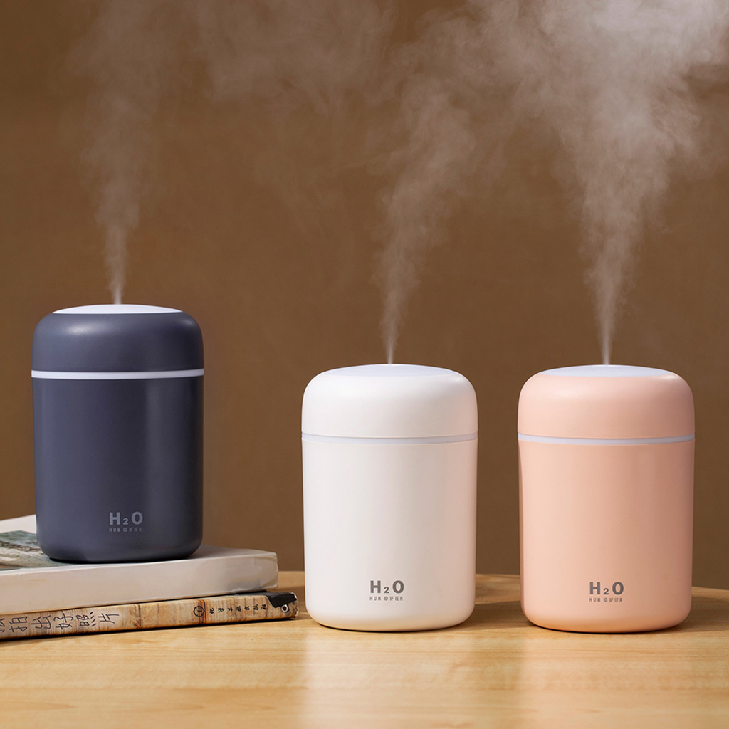Three H2O humidifiers in blue, white, and pink on a wooden surface with steam rising.