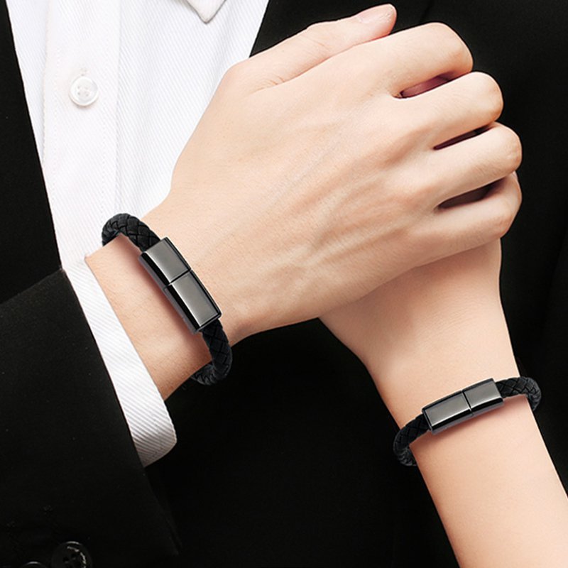 Person wearing two black bracelets on their wrists with a dark background