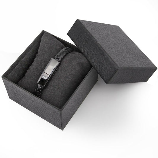 Black leather bracelet with metal clasp in a gray box on a white background